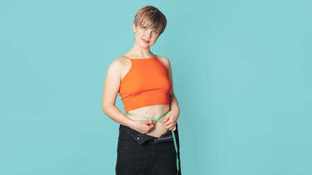 A happy slender woman in clothes with a measuring tape on a colored background. The concept of a healthy body, body positivity. Panoramic banner. Copy space.の写真素材