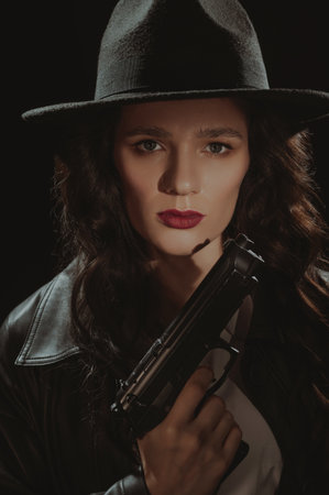 Close-up portrait of a female detective in a coat and hat with a gun in her hands. A book drama noir portrait in the style of detectives of the 1950s.の写真素材