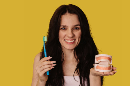 Caucasian young woman with a toothbrush and a jaw model on a yellow isolated background.の写真素材