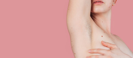 A young beautiful shirtless woman showing off her hairy armpits on an isolated pink background. Panoramic banner. A place for the text.の写真素材