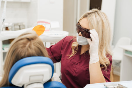 Professional female doctor uses ultraviolet lamp after making a filling on a tooth for joyful happy caucasian woman in modern dental cabinetの写真素材