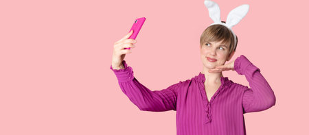 A beautiful girl with bunny ears on a colored background with a smartphone in her hands.の写真素材