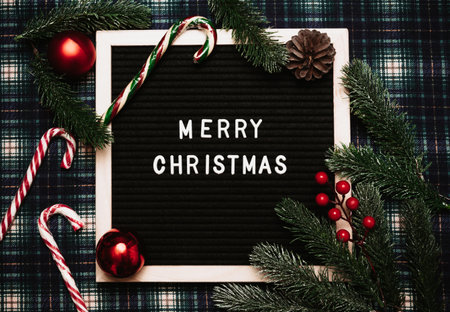 Merry Christmas lettering in plastic letters on an old vintage letter board. There are caramel canes, balls, cones and fir branches all around. Top view. Flatley. Ready-made Christmas greeting card.の写真素材