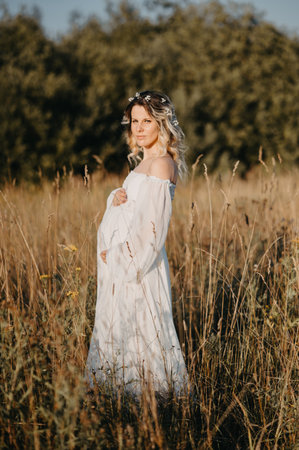 A young expectant mother in the third trimester of pregnancy in a white dress against the background of a natural landscape. The concept of future motherhood.の写真素材