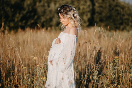 A young expectant mother in the third trimester of pregnancy in a white dress against the background of a natural landscape. The concept of future motherhood.の写真素材