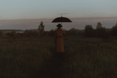 surreal silhouette of a man in a suit with an umbrella, standing in a raincoat in a field. The concept of freedomの写真素材