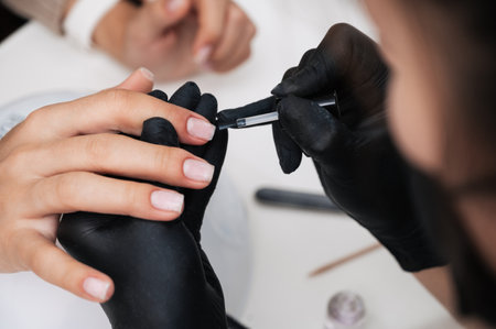 Manicure service. The manicurist paints her nails with a transparent gel polish. Applying nail polish. Well-groomed nails. A manicure master paints the nails of a client in a beauty salonの写真素材