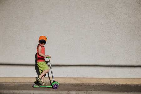 A little boy rides a scooter highlighted on a light wall. Open air. Minimalism.の写真素材
