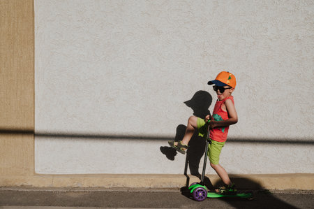 A little boy rides a scooter highlighted on a light wall. Open air. Minimalism.の写真素材