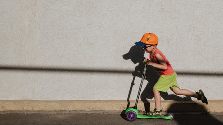 A little boy rides a scooter highlighted on a light wall. Open air. Minimalism. Panoramic banner.