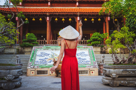Tourists in a red dress and a traditional Vietnamese headdress in the shape of a cone against the backdrop of a pagoda in Nha Trangの写真素材
