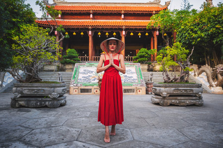 Portrait of a female tourist with her arms crossed over her chest in a traditional Vietnamese conical headdress against the backdrop of a pagoda in Nha Trangの写真素材