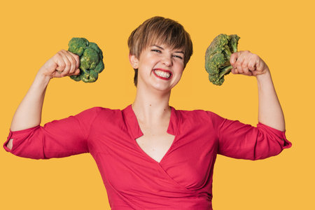 Broccoli in the hand of a smiling woman on a yellow background. healthy lifestyle.の写真素材