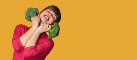 Broccoli in the hand of a slender smiling woman on a yellow background. A panoramic banner with a place for your text. healthy lifestyle.の写真素材