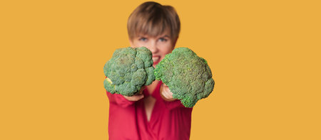 Broccoli in the hand of a slender smiling woman on a yellow background. A panoramic banner with a place for your text. healthy lifestyle.の写真素材