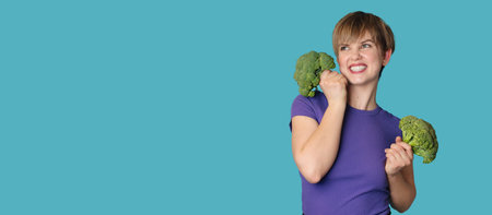 Broccoli in the hand of a slender smiling woman on a blue background. A panoramic banner with a place for your text. healthy lifestyle.の写真素材