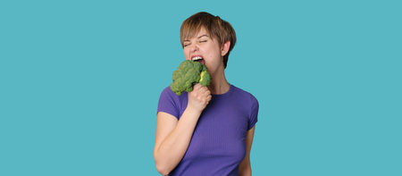 Broccoli in the hand of a slender smiling woman on a blue background. A panoramic banner with a place for your text. healthy lifestyle.の写真素材