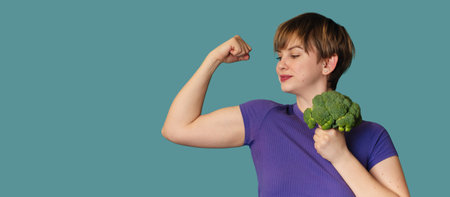 A happy, excited, funny young Caucasian woman doing exercises with broccoli dumbbells, standing against an isolated background, smiling. A panoramic banner with a place for text.の写真素材