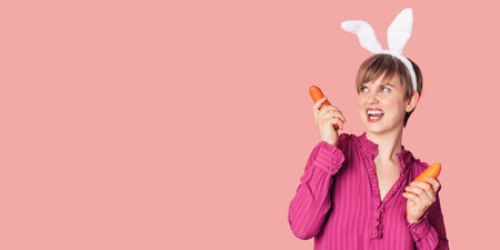 Smiling slender Caucasian girl in bunny ears with fresh carrots in her hands. Panoramic banner, free space. Organic vegetables.の写真素材