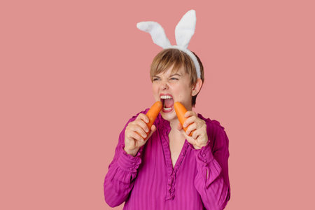 Smiling slender Caucasian girl in bunny ears with fresh carrots in her hands. Organic vegetables.の写真素材