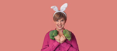 Studio shot of a young Caucasian woman in bunny ears holding fresh broccoli in her hands. healthy eating. A panoramic banner with copy space.の写真素材