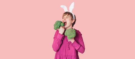 Smiling slender Caucasian girl in bunny ears with green broccoli in her hands, free space. Organic vegetablesの写真素材