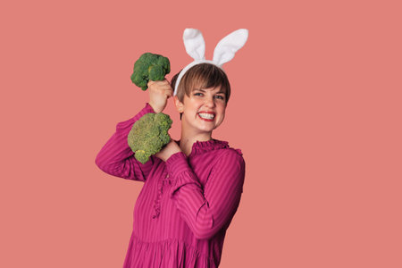 Studio shot of a young Caucasian woman in bunny ears holding fresh broccoli in her hands.の写真素材