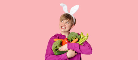 Studio shot, a young Caucasian woman in bunny ears holding a lot of organic and fresh vegetables in her hands. healthy eating.A panoramic banner with a copy of the space.の写真素材