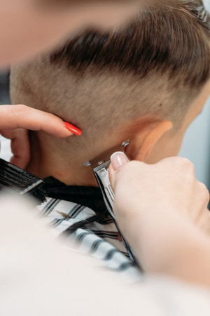 A female hairdresser cuts a little boys hair with a hair trimmer. Close-up.