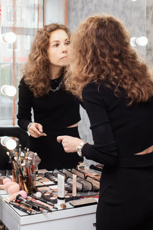 Beautiful girl is doing a makeup, retouching eyebrows while looking at the mirrorの写真素材
