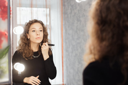 A young woman applies makeup in a home bathroom. She looks at herself in the mirror while powdering her faceの写真素材