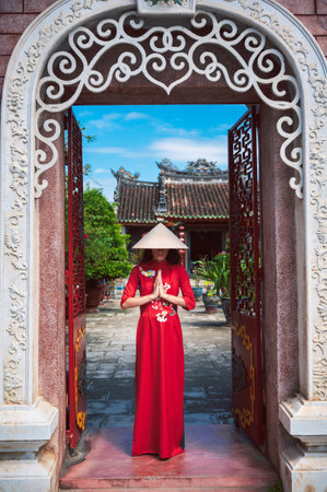 A female tourist in a traditional Vietnamese hat and traditional dress, visiting a Buddhist temple