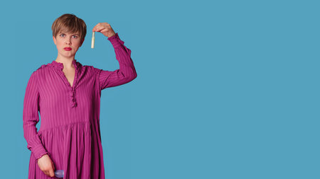A Caucasian woman dressed in casual clothes holds a tampon in her hands, highlighted on a blue background.の写真素材