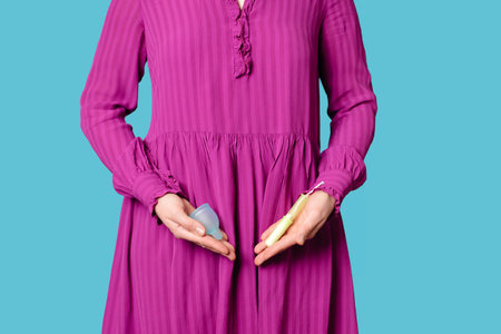 A young woman holds a tampon and a silicone menstrual cup against the background of her stomach.の写真素材