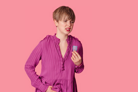 A young woman holds a silicone menstrual cup against the background of her aching belly.の写真素材