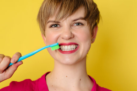 A young Caucasian woman with an amazing smile with a toothbrush in her hands on a yellow isolated background.の写真素材