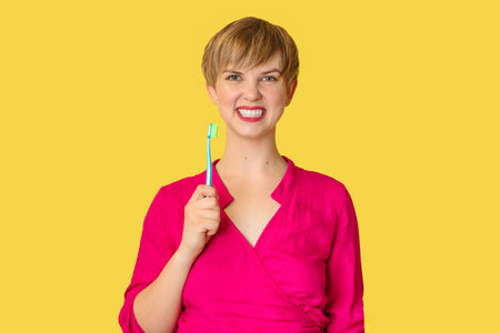 A smiling woman with healthy teeth holds a toothbrush in her hands. A young beautiful girl on a bright background. Oral hygiene.の写真素材