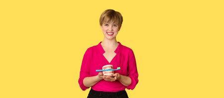 A young Caucasian woman with an amazing smile with a toothbrush and a jaw model in her hands on a yellow background. A place for your text.の写真素材