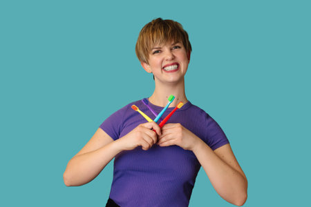 A smiling woman with healthy teeth holds a set of bright toothbrushes on a bright background. Oral hygiene.の写真素材