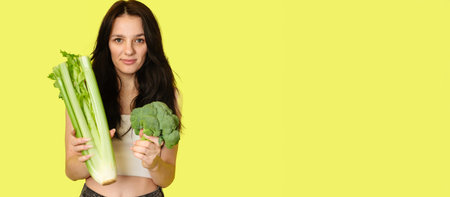 Smiling slender Caucasian girl with green vegetables in her hands, broccoli and celery, free space. Organic vegetables.の写真素材