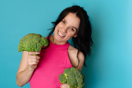 A studio shot of a young woman holding fresh broccoli in her hands. The concept of healthy foodの写真素材