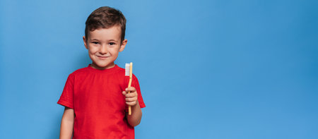 A smiling boy with healthy teeth holds a plus tooth and a toothbrush on a blue isolated background. Oral hygiene. Pediatric dentistry. Prevention of caries. A place for your text.の写真素材