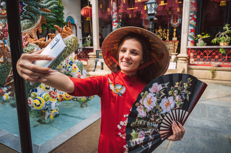 A young woman with Ao Dai dress takes a selfie in temple in Hoi An, Vietnam.の写真素材