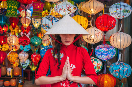 A woman in traditional Vietnamese clothes and a Non La hat on the background of lanterns in the ancient city of Hoi An.の写真素材