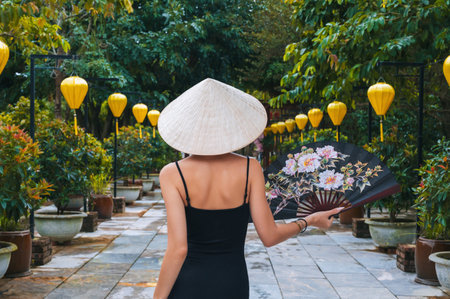 A woman in a traditional Vietnamese hat on the background of an Asian cultural garden decorated with lanternsの写真素材