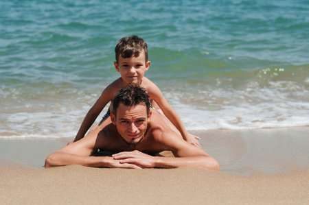 A happy father and son are lying on the sand.の写真素材