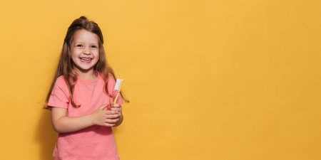 A happy girl is holding a toothbrush in her hands. An isolated panoramic shot. A place for your text. Pediatric dentistryの写真素材