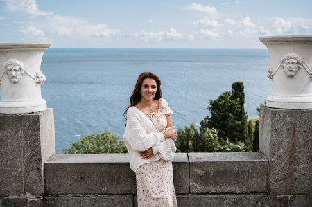 A young tourist girl in a vintage white dress poses near the palace. The sea is behind her. A snapshot from recreation and excursionsの写真素材