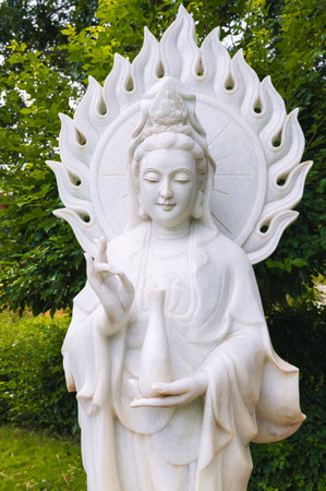 White Buddha statue surrounded by tropical plants in a garden in Asia.の写真素材