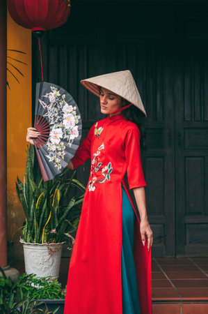 A woman in a traditional Vietnamese costume, a conical hat on the background of a building in a traditional Asian style.の写真素材